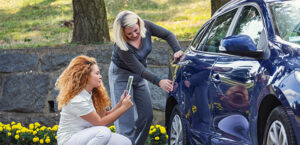 A mother and daughter looking at damage to the side of a car, while taking pictures of the damage with a smartphone