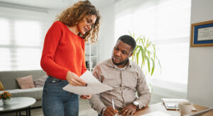 Standing woman holding insurance documents in her hands explaining them to a sitting male