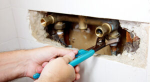 A close-up of hands fixing the plumbing damage on a pipe behind a wall.